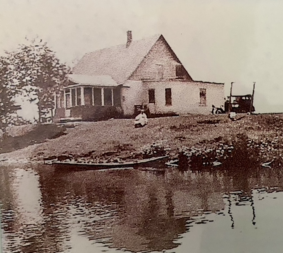 A child in a flowing white frock plays in the grass in a sepia-toned photo of the old Hansen homestead, circa 1930, at Hansen Lake near Park Falls, Wisconsin.